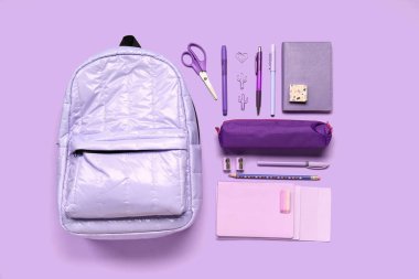 Kalem kılıflı şık okul çantası ve leylak arka planda farklı kırtasiye malzemeleri.