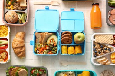 Farklı lezzetli yemekleri ve bej fayanslı bir şişe meyve suyu olan birçok beslenme çantası.