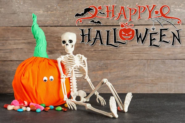 Halloween greeting card with decorative pumpkin, skeleton and candies on wooden background