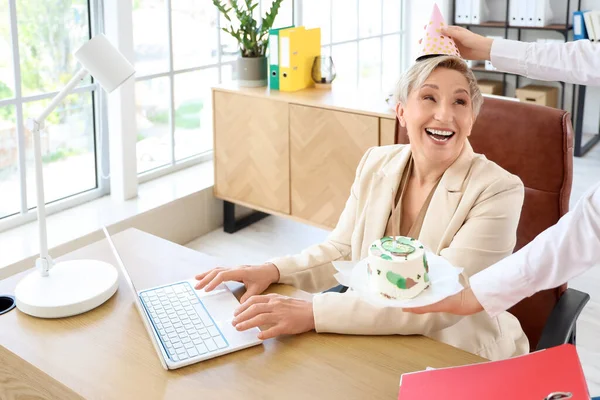 Mature woman receiving birthday cake from colleague in office