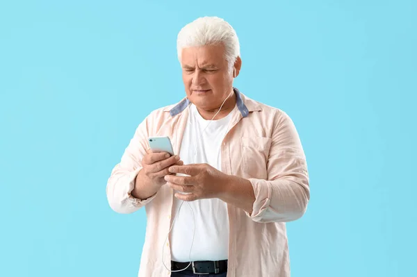 戴耳机的老年人用蓝色背景的手机 — 图库照片