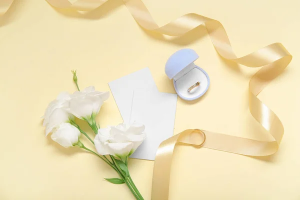 Box with wedding ring, blank cards, ribbon and flowers on color background