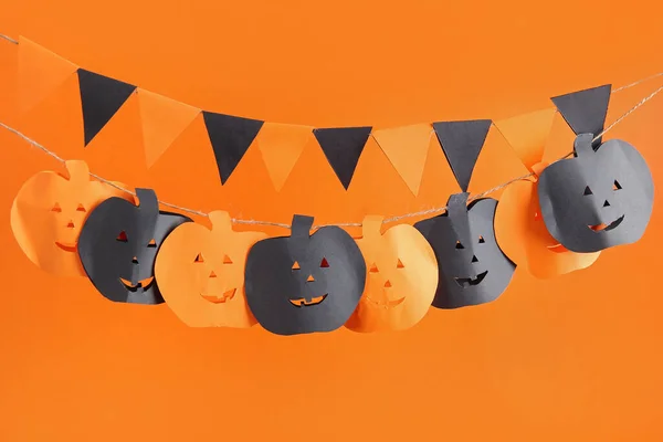 Garlands made of paper flags and pumpkins for Halloween celebration on orange background