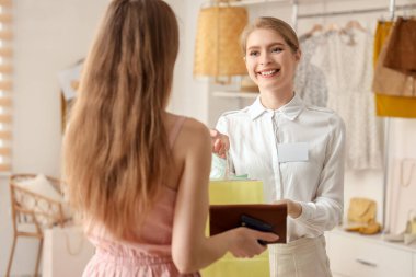 Kadın satıcı butikteki müşterilere alışveriş torbaları veriyor.