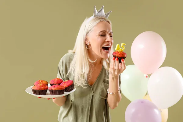 Mature woman with birthday muffins on green background