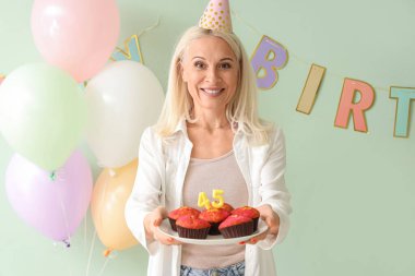 Yeşil arka planda doğum günü çörekleri olan olgun bir kadın.