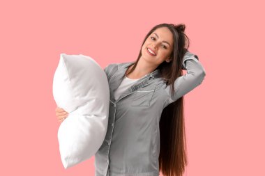 Pembe arka planda yastıklı pijamalı güzel bir kadın.