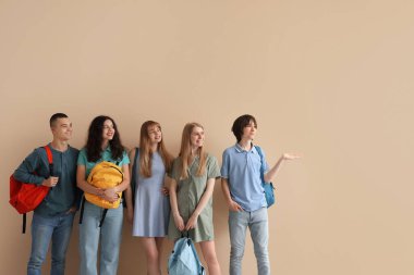 Bej duvarın yanında sırt çantalı bir grup öğrenci.