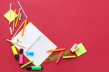 Kırmızı arkaplanda boş defter ve farklı kırtasiye malzemesi olan kompozisyon