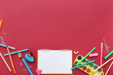 Kırmızı arkaplanda boş defter ve farklı kırtasiye malzemesi olan kompozisyon