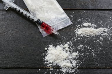 Koyu ahşap arka planda uyuşturucu ve şırınga dolu plastik torba.