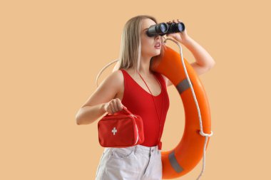 Dürbünlü kadın cankurtaran, ilk yardım çantası ve bej arka planda yüzük şamandırası.