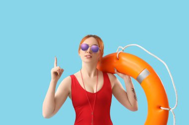 Yüzük şamandıralı kadın cankurtaran mavi arka plandaki bir şeyi işaret ediyor.