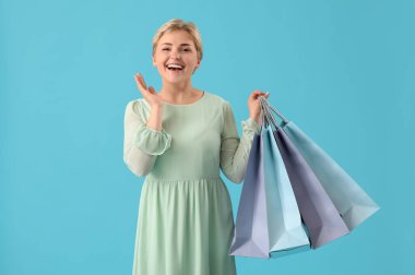 Mavi arka planda alışveriş torbaları olan mutlu, güzel bir kadın.