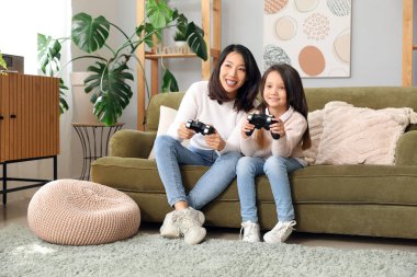 Asyalı anne ve küçük kızı evde video oyunu oynuyorlar.
