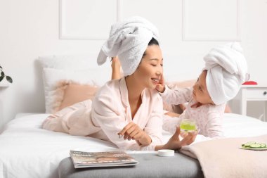 Asyalı anne ve küçük kızı yatak odasında yüz kremi sürüyorlar.