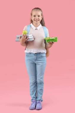 Beslenme çantası, elma ve pembe arka planda kitapları olan mutlu küçük kız.