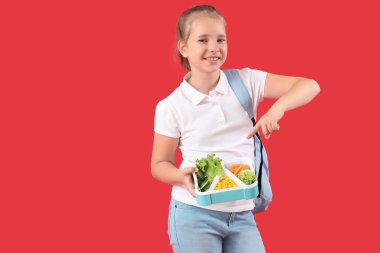 Kırmızı arka plandaki beslenme çantasını gösteren mutlu küçük kız.