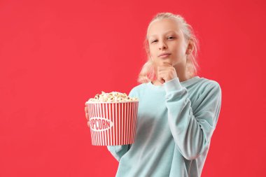 Kırmızı arka planda patlamış mısırı olan düşünceli bir kız.