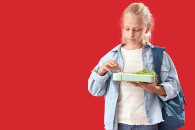 Sırt çantası ve kırmızı arka planda beslenme çantası olan mutlu bir kız.