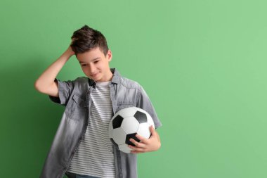 Yeşil arka planda futbol topu olan üzgün küçük çocuk.