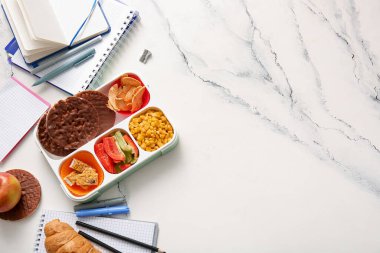 Lezzetli yemekleri ve grunge beyaz arka planda farklı kırtasiyeleri olan beslenme çantası.