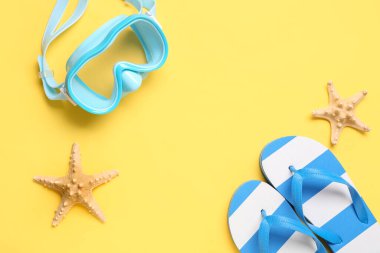 Yüzme maskesi, denizyıldızı ve sarı arka planda parmak arası terlikler.