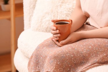 Evdeki kanepede bir fincan lezzetli kahveyle dinlenen kadın.