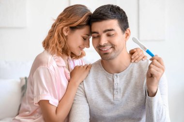 Yatak odasında hamilelik testi olan mutlu genç çift.