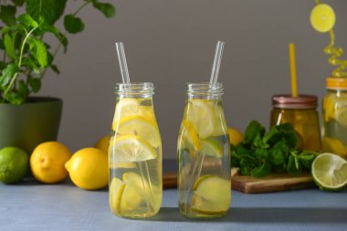Limonlu ve naneli limonata şişeleri mavi masada.