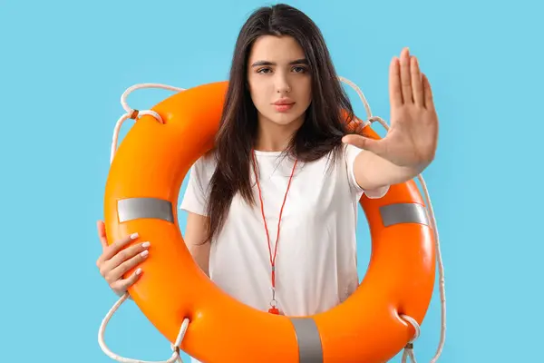 Female lifeguard with ring buoy showing stop gesture on blue background
