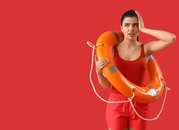 Shocked female lifeguard with ring buoy on red background