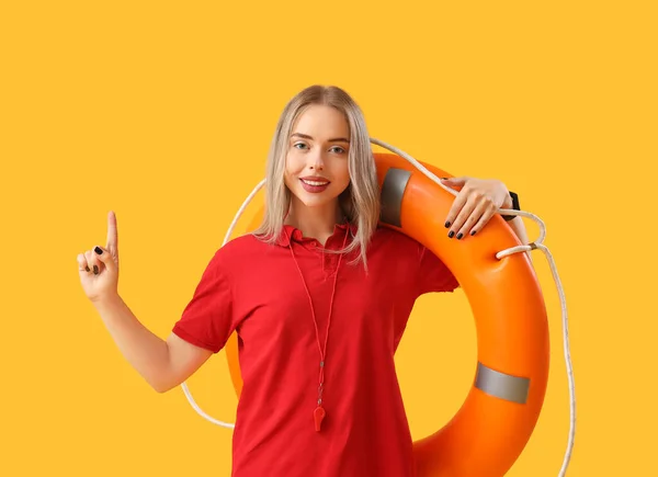 Female lifeguard with ring buoy pointing at something on yellow background