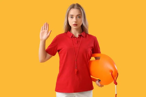 Female lifeguard with rescue buoy showing stop gesture on yellow background