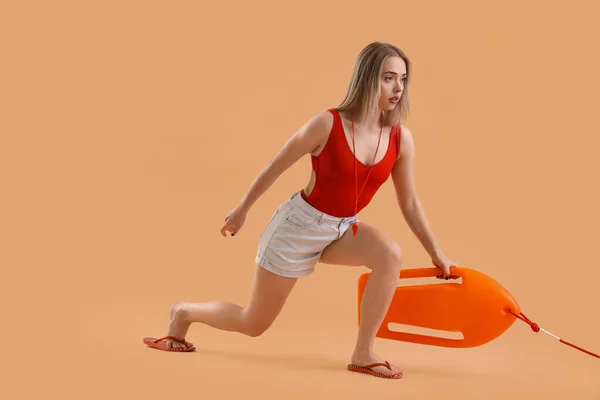 Female lifeguard with rescue buoy on beige background