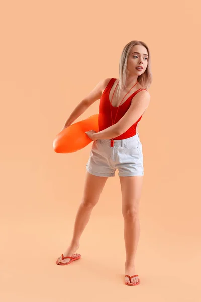 Female lifeguard with rescue buoy on beige background