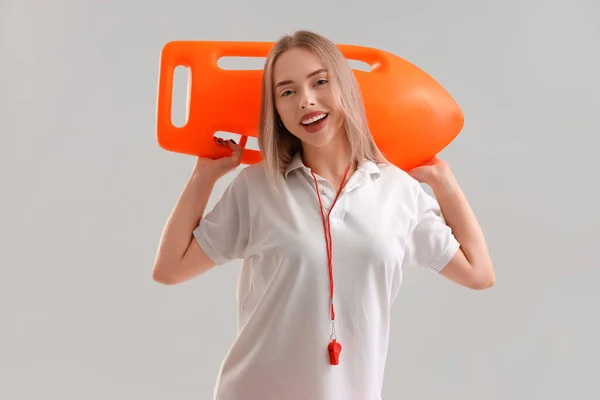 Female lifeguard with rescue buoy on light background