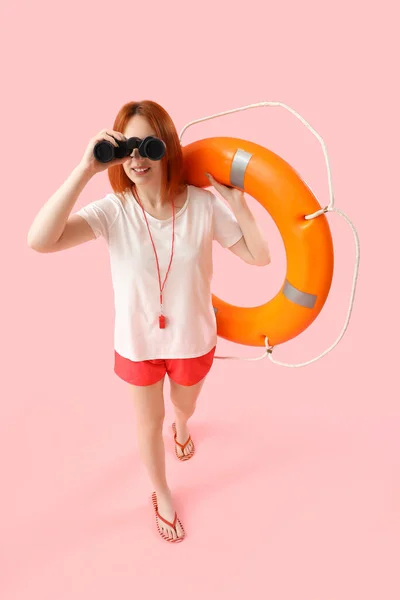 Female lifeguard with ring buoy and binoculars on pink background