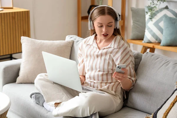 Young woman in headphones with laptop and mobile phone working at home