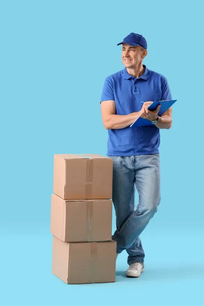 青い背景にクリップボードと小包が付いている成熟した宅配業者 — ストック写真
