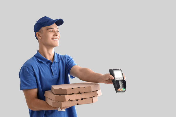 Young courier with pizza and payment terminal on light background