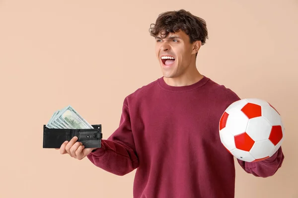 ベージュのバックグラウンドにサッカーボールと財布を持つ若い男 スポーツベットコンセプト — ストック写真