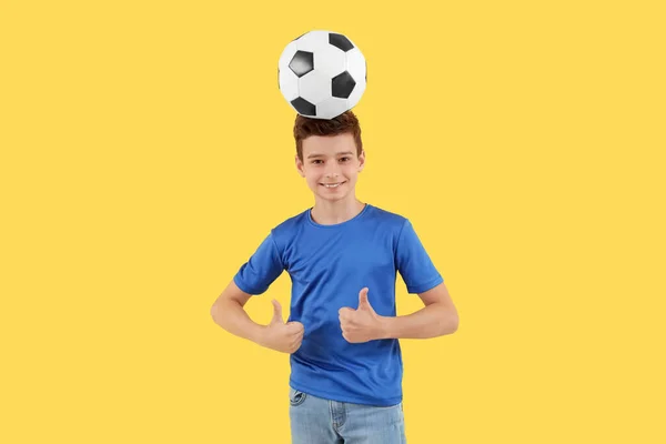 黄色の背景に親指を示すサッカーボールを持つ小さな少年 — ストック写真