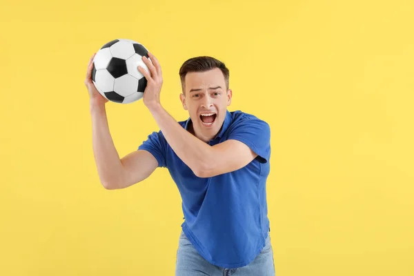 黄色い背景にサッカーボールを持つ感情的な若者 — ストック写真