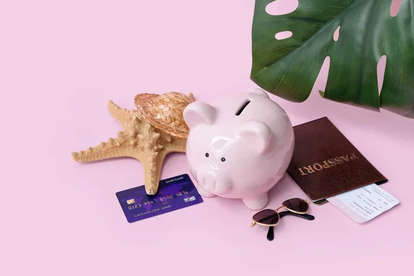 Piggy bank with beach accessories, credit card and passport on pink background. Concept of savings for travel