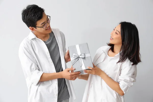 Young Asian friends with gift on light background