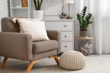 Aydınlık oturma odasının iç tarafında yastıkları olan rahat gri bir koltuk.