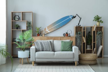 Sörf tahtası, raf ünitesi ve kanepesi olan bir oturma odası.