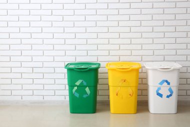 Beyaz tuğla duvarın yanında geri dönüşüm sembolü olan farklı çöp bidonları