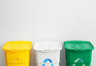 Beyaz duvarın yanında geri dönüşüm sembolü olan farklı çöp bidonları